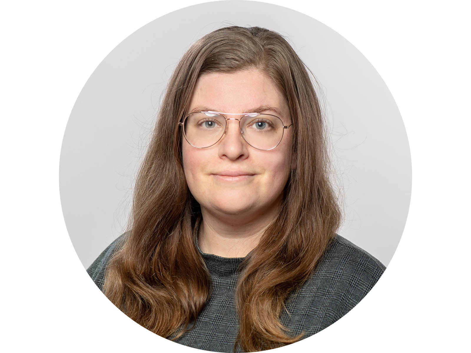 A light-skinned woman with long, reddish-dark blonde hair, blue eyes, and glasses. She smiles at the camera and is wearing a gray plaid mock-neck top.