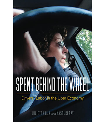 The cover of Spent Behind The Wheel is a view of an Uber driver as seen through the steering wheel. They are wearing sunglasses and turned to look out the driver’s side window. Their hand is on the top of the steering wheel, mid-turn.
